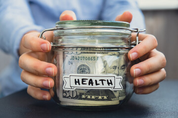 Female hands Glass jar full of American currency dollars cash banknote with text HEALTH....