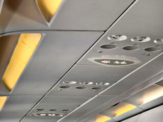 Close-up of commercial airplane ceiling showing light panels, air vents, and passenger service units. Ideal for travel, aviation, and airline concepts.