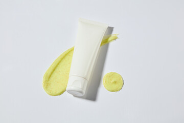 Minimalist style advertising photo with a blank label tube and yellow exfoliating scrub smear on...