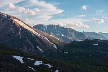 Golden sunset lit glacier on big rocky steep slope. Green mountain pass with snowfields against...