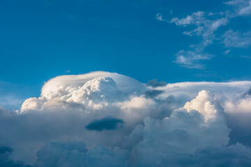 Huge dramatic lenticular cloud on white lush cloudy hill in blue sky. Beautiful cloudscape with big...