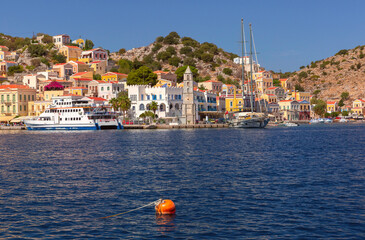 Naklejka premium Sunny View of Ano Symi with colorful houses and Clocktower, Dodecanese islands, Greece