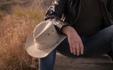Adult man sitting on tree trunk on wild with cowboy hat on knee