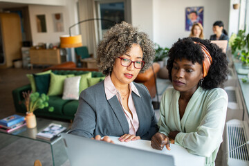 Two businesswomen discussing work with a laptop at a modern office