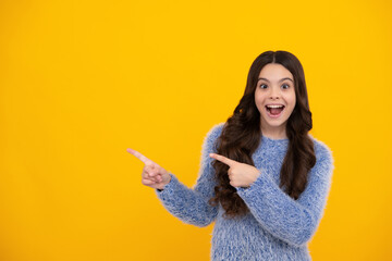 Happy teenager, positive and smiling emotions of teen girl. Portrait of cute teenager child girl pointing hand showing adverts with copy space over yellow background.