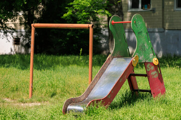 A rusty old playground slide sits in a grassy field next to a metal pole