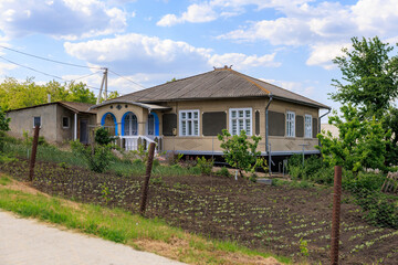 A house with a blue door and white windows sits on a dirt field
