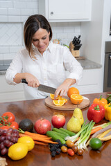 Friendly looking woman with brown bob chopping fruit in kitchen