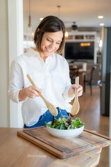 Cute middle aged woman mixing a salad in her kitchen with wooden spoons