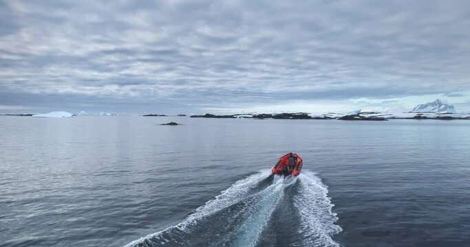 Man riding zodiac boat in Antarctica polar ocean pov. Red motorboat fast cross coastline bay. Towering snow covered mountains icebergs in the background. People enjoy Antarctic travel and exploration