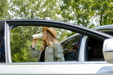 Blonde woman stoped on road next to car and drink coffee or tea from reusable mug. Refuse reuse...
