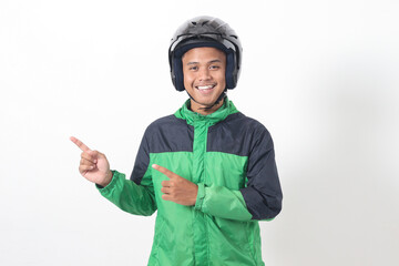 Portrait of Asian online taxi driver wearing green jacket and helmet pointing at empty space with finger. Isolated image on white background
