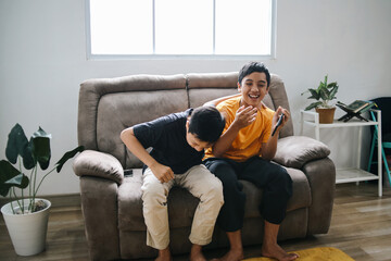 Potrait Of Funny Two Young Boys Sitting On The Sofa Laughing Out Loud While Holding Smartphone...