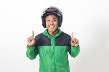 Portrait of Asian online taxi driver wearing green jacket and helmet pointing at empty space with finger. Isolated image on white background