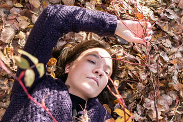 Young woman enjoying nature lying peacefully surrounded by autumn leaves.