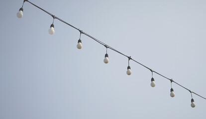 Hanging outdoor light bulbs against the sky background minimal style.