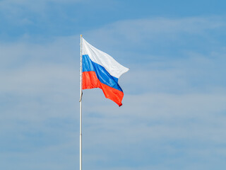 Russian tricolor flag waving in the wind against a blue sky.