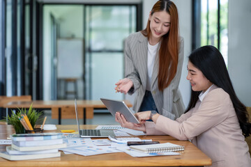 Two Asian businesswomen working Creative discussion in office using laptop and tablet, business concept