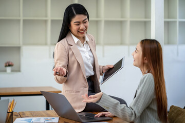 Two Asian businesswomen working Creative discussion in office using laptop and tablet, business concept