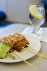 A plate of traditional Malaysian chicken sate skewers with peanut sauce, rice cakes, sliced cucumber red onion, served as an appetiser on a business class flight from Sydney to Kuala Lumpur