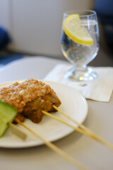 A plate of traditional Malaysian chicken sate skewers with peanut sauce, rice cakes, sliced cucumber red onion, served as an appetiser on a business class flight from Sydney to Kuala Lumpur