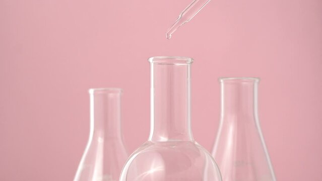 Macro video of dropper & beaker on plain background. Close up of scientific lab equipments on coloured background.