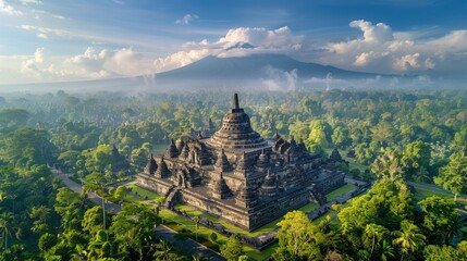 Aerial view of the Borobudur Temple in Indonesia, showcasing the massive Buddhist temple complex surrounded by lush green landscape and distant volcanoes.     