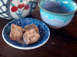 Tea time on Yakushima, Natural lump cane sugar on ceramic plate, tea cup and pot served on wooden table