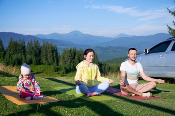 Young family doing yoga outdoors in scenic mountainous landscape in morning. Father, mother and...