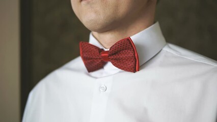 A young man in a white shirt adjusts his red bow tie with his hands. A musician gets dressed before a concert. A host backstage before going on stage. A businessman at a meeting.