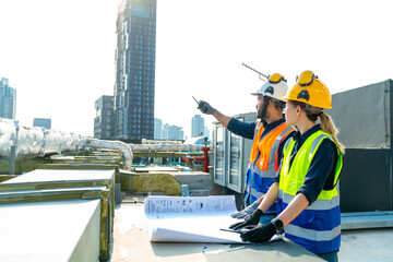 Professional Asian man and woman teamwork engineer and foreman using blueprint working outdoor at construction site building rooftop. Architecture inspector inspect building exterior structure system.