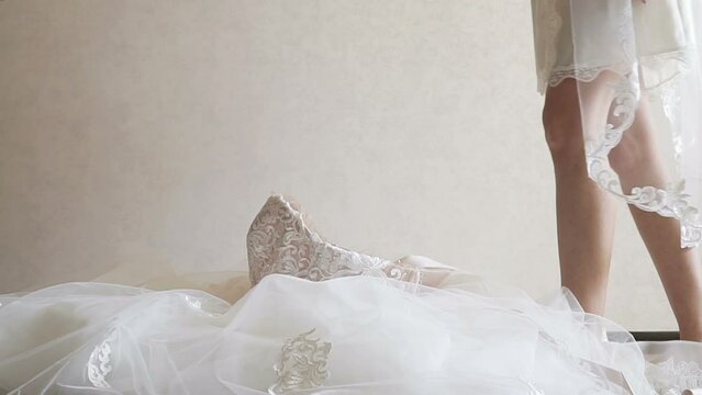 The bride steps barefoot into her wedding dress. The bride getting ready in the morning. Wedding day. Women's feet. Toes touch the floor.