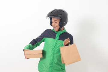 Portrait of Asian online courier driver wearing green jacket and helmet giving craft paper shopping bag and box package. Isolated image on white background
