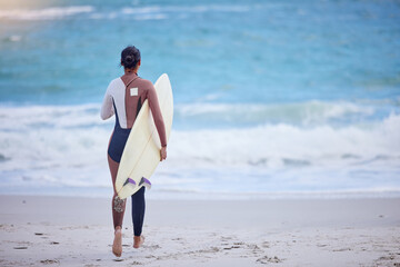 Girl, walking and board for surfing at beach, workout and training for water sports competition. Female person, back and travel to ocean or sea for waves, fitness and athlete for exercise in nature