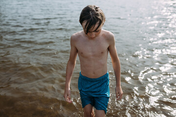 Preteen boy walking out of lake water in summer