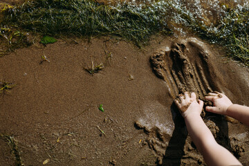 Child's hands playing with sand by the lake shore