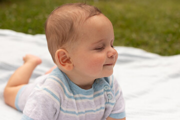 Smiling baby boy lying on a blanket outdoors, enjoying a sunny day