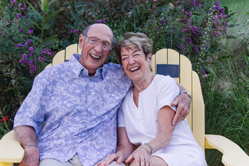 Laughing elderly couple on a garden bench surrounded by flowers