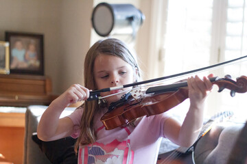 Young girl deeply focused on playing violin indoors.