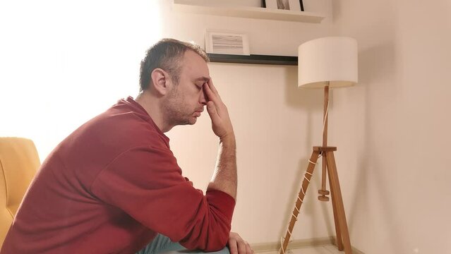 Man with headache sitting on a sofa at home.