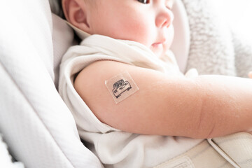 Band-aid with character on it on baby's right arm with red skin after vaccination