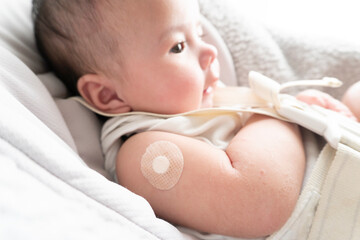 Band-aid on baby's right arm with red skin after vaccination