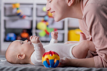 Young mother talks and plays with her baby son while lying on her back. Baby care, motherhood...