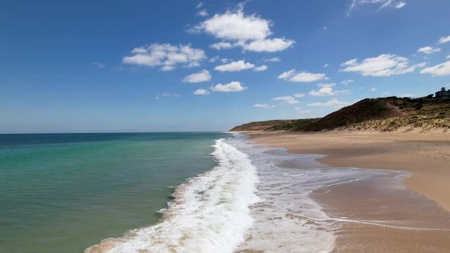 A drone flying along a beautiful beach in South Australia as the small waves roll against the shore. This long stretch of beach is Port Willunga in Australia, which is a beautiful scenic landscape.