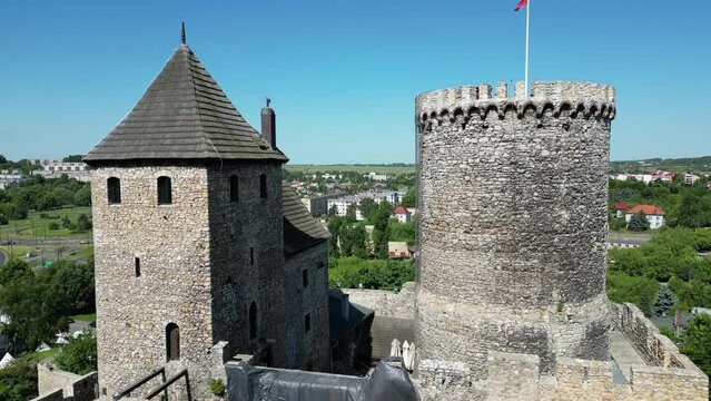 Medieval Bedzin castle with a turret, walls, and courtyard during a beautiful summer day surrounded by lush greenery, grass, and trees under a clear blue sky.