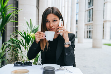 professional woman having a conversation over the phone while enjoying a cup of coffee at an...