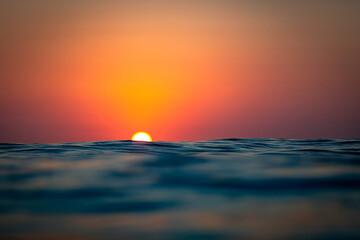 Golden sun orb rising above a dark blue rippled sea © Nautilus Creative