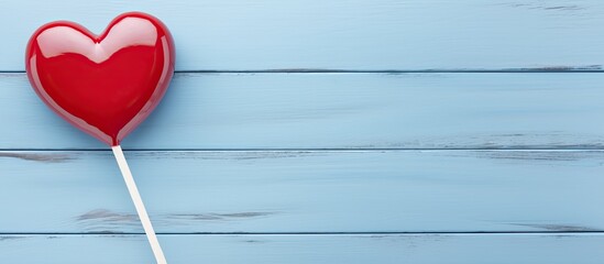 Close up of a Valentine s Day heart shaped lollipop and a white frame on a blue wooden background with copy space image