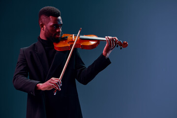 Soulful African American Man in Black Suit Playing Violin Against Dark Background