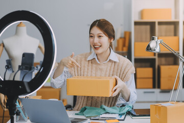 Young woman freelancer working sme business online shopping and packing clothes with cardboard box...